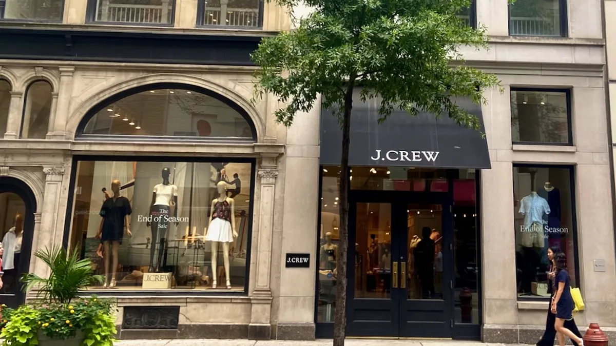 People walking past a clothing store. A tree in front of the main entrance.