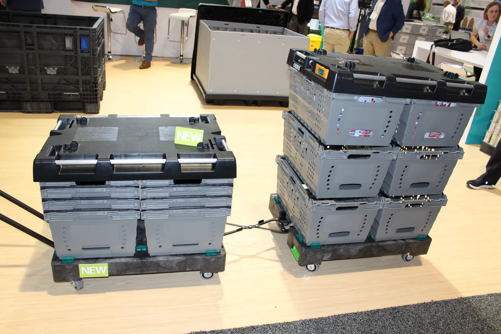 A stack of gray plastic bulk containers on a black pallet and moveable hand cart.