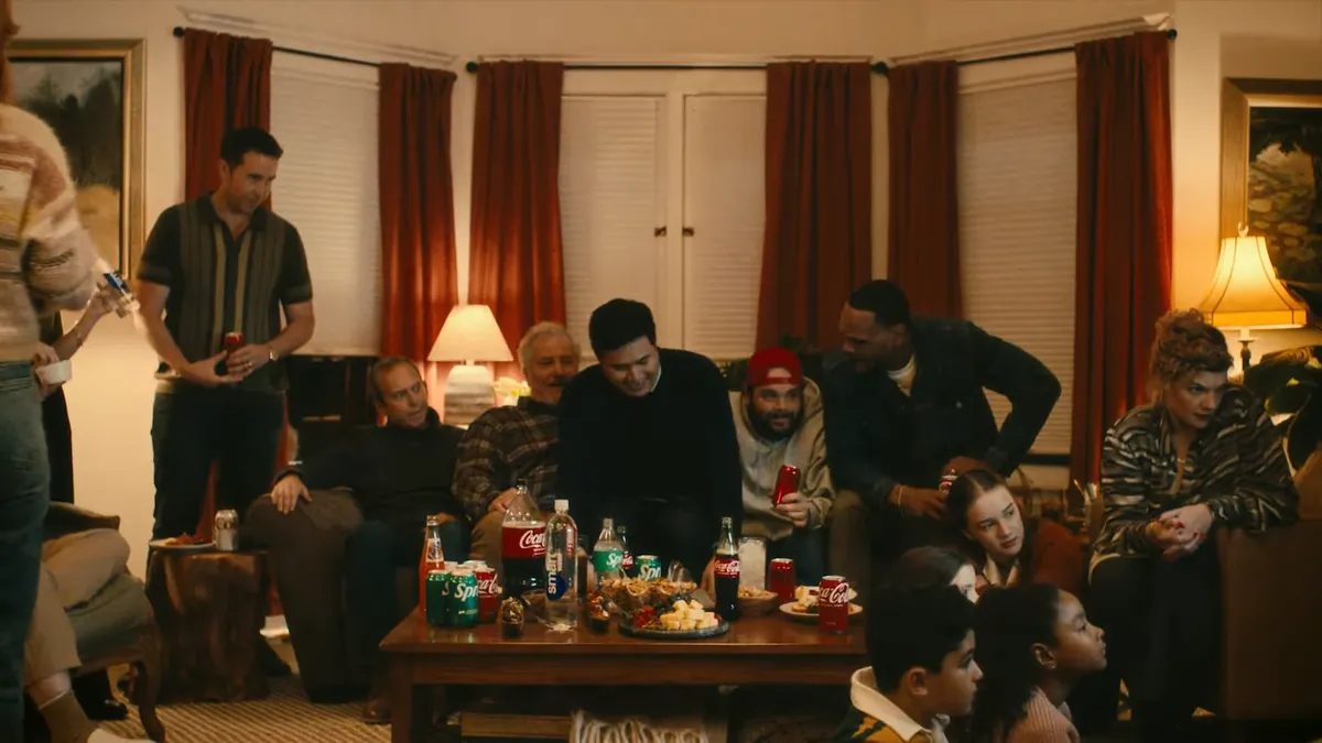 A group of people gather in a living room with Coca-Cola products on a table