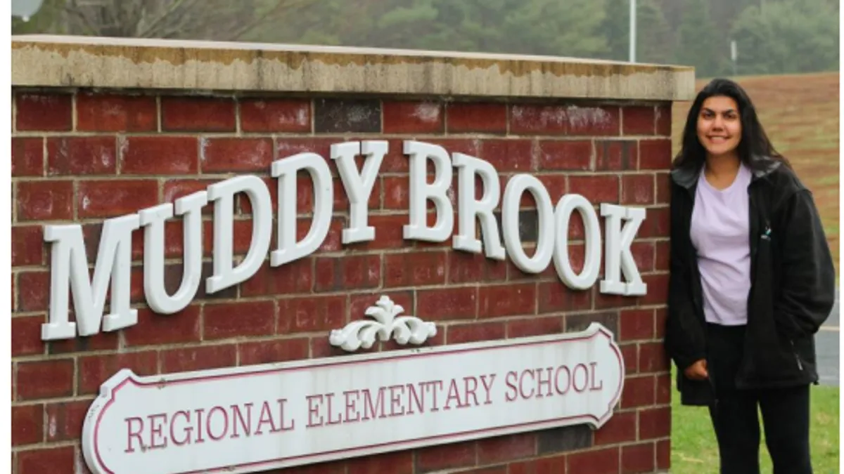 High school student stands next to outdoor elementary school sign.