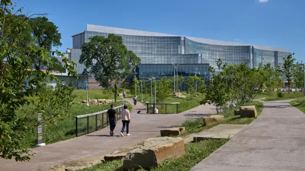 People walking on pedestrian pathways in green space surrounding Ford's new global headquarters, which is visible in the background.