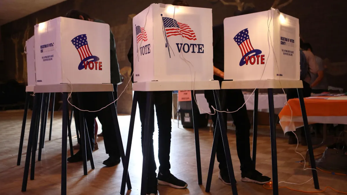 three people stand behind voting booths