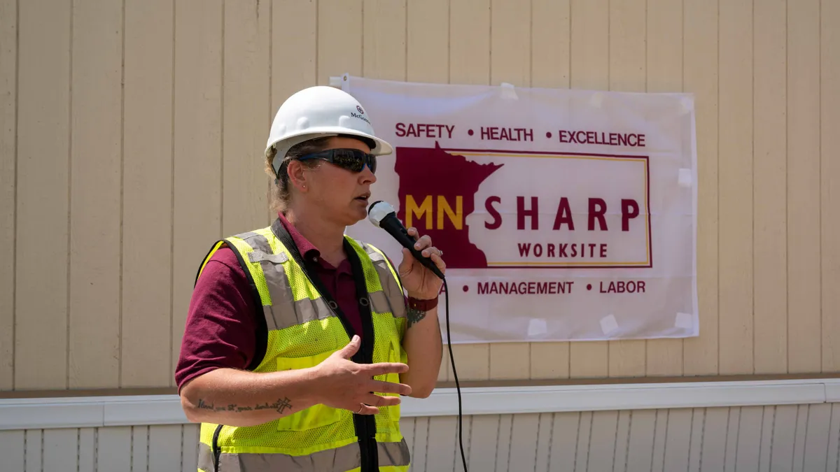 A woman stands at a microphone on a jobsite