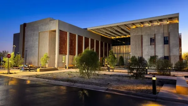 A building at night lit up by lights up front. It is large, brown and blocky.