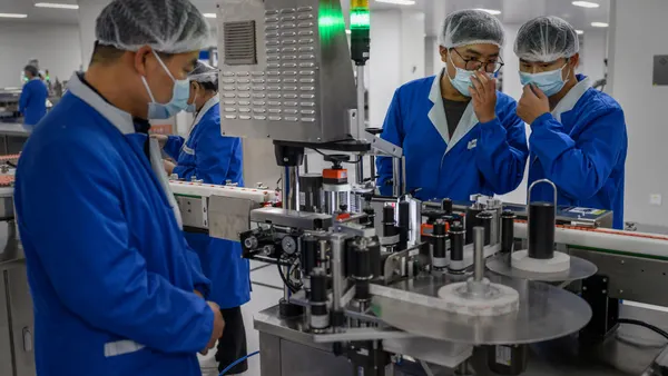 Three laboratory technicians stand over a machine that labels drug vials.