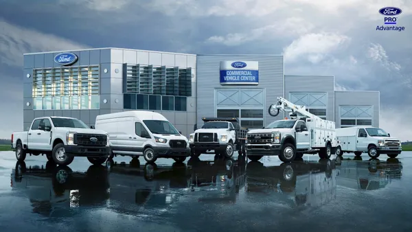 A lineup of white Ford commercial trucks parked in front of a Ford Commercial Vehicle Center.