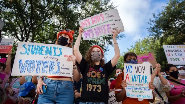 Protestors with face coverings and signs advocating for reproductive and voting rights stand among crowd of other protestors.