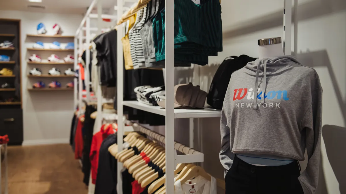 A grey hoodie on a mannequin reads "Wilson," with racks of clothing in the background.