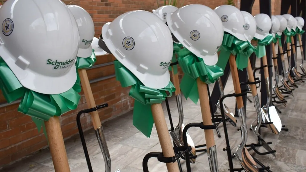 Row of white hard hats with green ribbons placed on shovels for a groundbreaking ceremony.