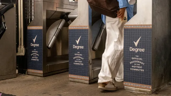 Commuters pass through a row of New York City subway turnstiles that feature ads from Degree.
