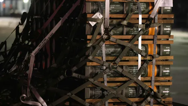 A cargo pallet filled with rockets and covered in safety straps sits on a tarmac at night.