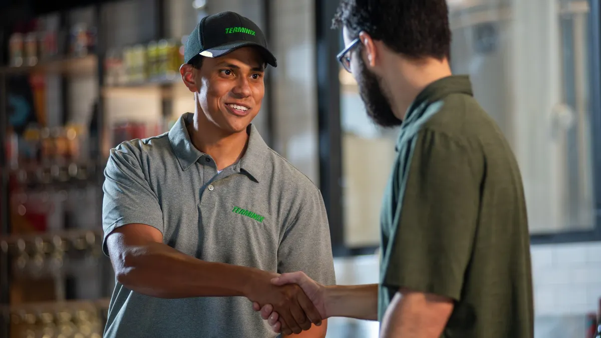 A Terminix technician shakes hands with a customer in a store-like setting.