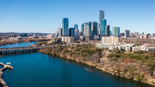Bridge over blue body of water with city skyline in background.
