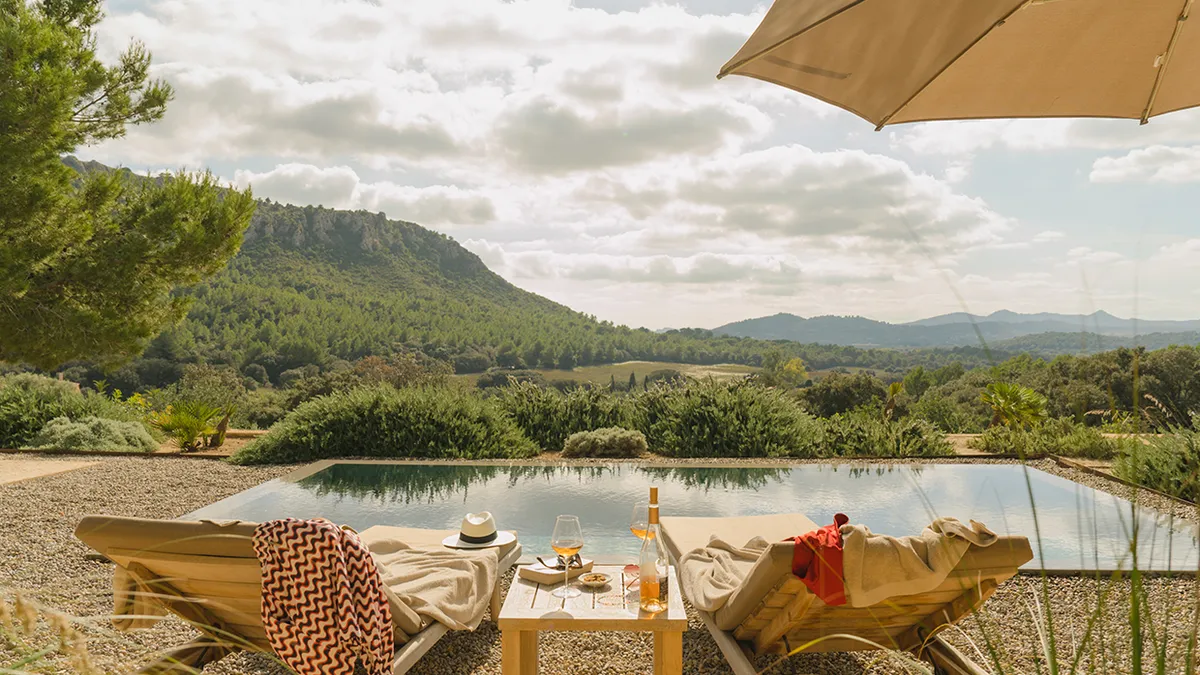 Two empty lounge chairs in front of a pool overlooking a vast hilly region.