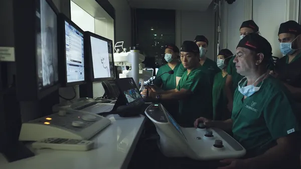 Neurosurgeon Vitor Mendes Pereira performs a robotic aneurysm procedure while seated at a console in Panama as other clinicians observe.