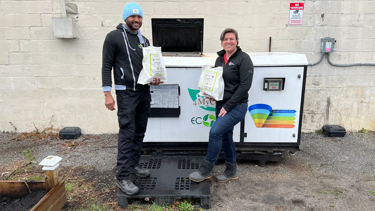 Photo of two people holding compost bags next to an organics processing machine outside