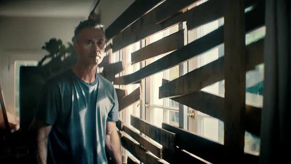 Actor Freddie Prinze Jr, wearing a dark gray shirt,, boards a window shut with wooden planks in a video for DoorDash.