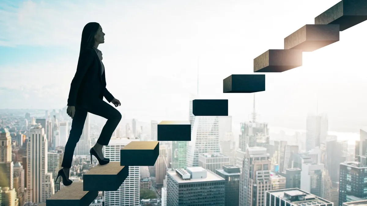 Road to success concept with businesswoman going up the stairs on sunny megapolis city background