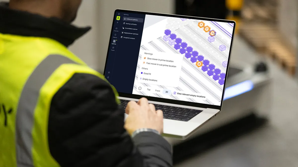 A worker in a high-visibility vest uses a laptop displaying warehouse optimization software.