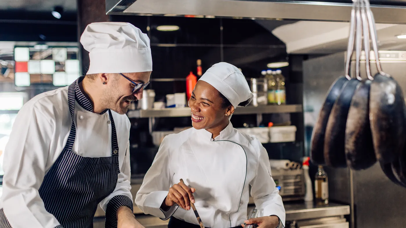 Two chefs smiling and cooking in a restaurant kitchen.