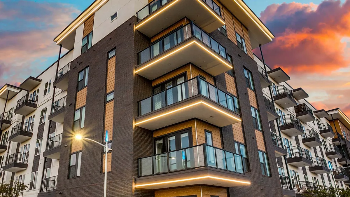 Five-story brown, modern apartment building with balconies on the corner.