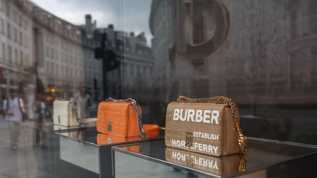 Burberry handbags sit in a store window reflecting a grey day.