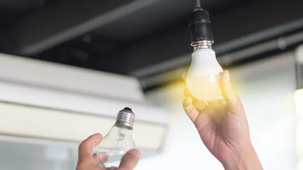 A closeup shot showing the hand of a man who is replacing a compact-fluorescent bulb with a new LED light fixture.