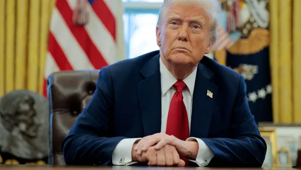 Donald Trump sits at his desk in the Oval Office with his hands clasped.