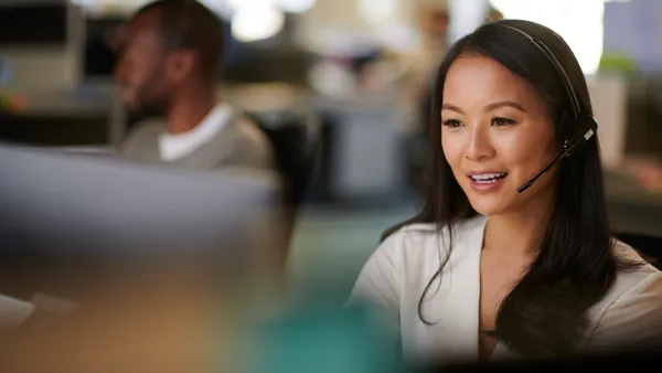 A woman talks on a headset in front of a computer.