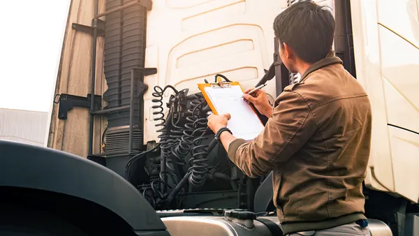 Person holding a clipboard, piece of paper and a pen while looking at the back of a truck.