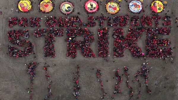 An aerial view shows protesters dressed in red spelling standing in formation to spell out "For our students, strike" on a beach.