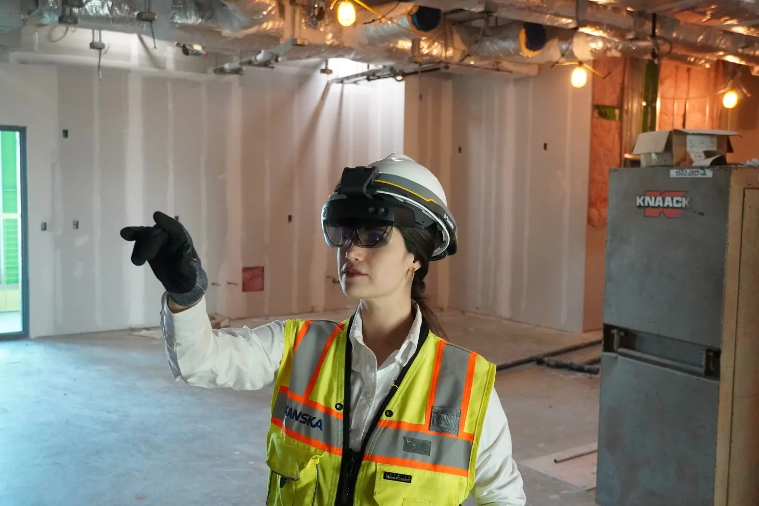 A person wears personal protective equipment and stares forward with a finger outstretched, with virtual reality gear on their head.