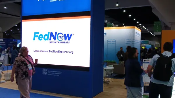 A digital display on a conference trade floor advertising the Federal Reserve's instant payments system FedNow with a person walking past.