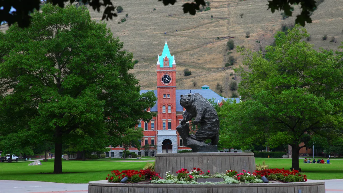 A metal bear statue in the foreground, a brick academic building in the mid ground, and mountains in the background