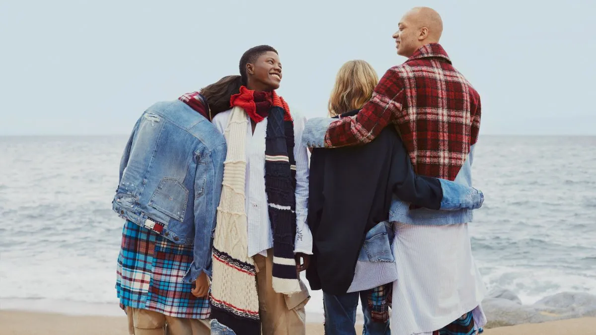 A group of four people stand on a beach, posing for a picture, wearing the Tommy Hilfiger and Greg Lauren collection.