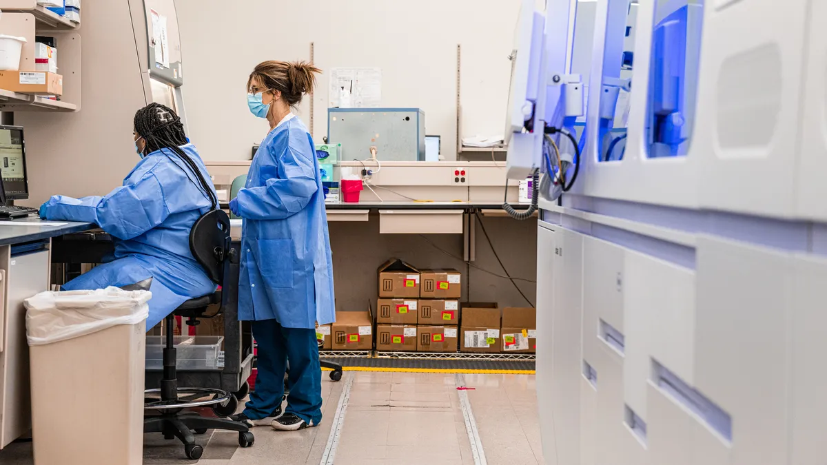 Deira Ward (L) and Lisa Bates (R) work at a computer near a large PCR analysis machine at a Quest Diagnostics testing lab in Indianapolis, Indiana. The lab is capable of processing up to 3700 tests pe