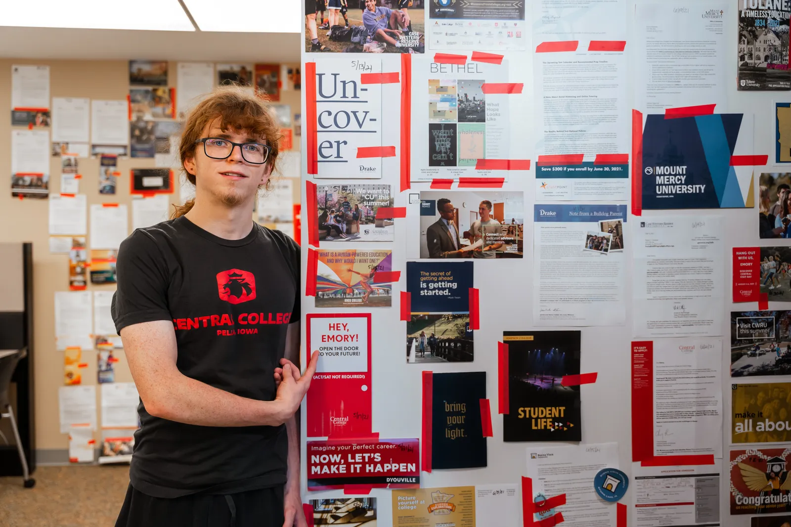 Someone stands next to college admissions materials taped to a wall.