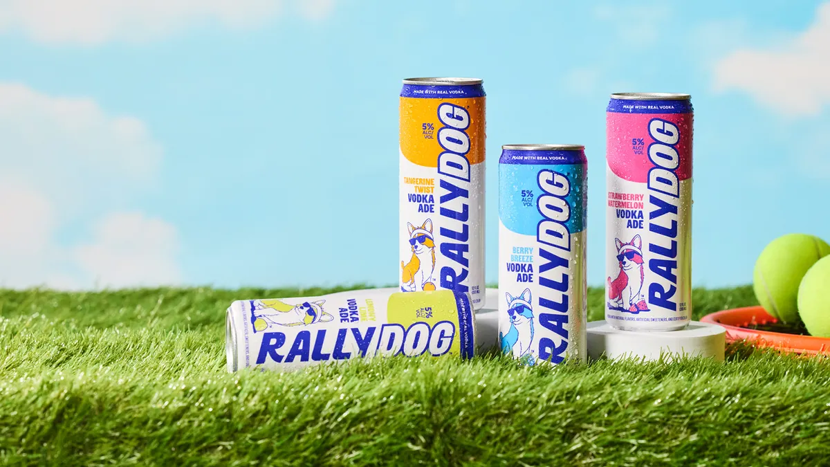Cans of Rally Dog are on a turf with tennis balls in the background.
