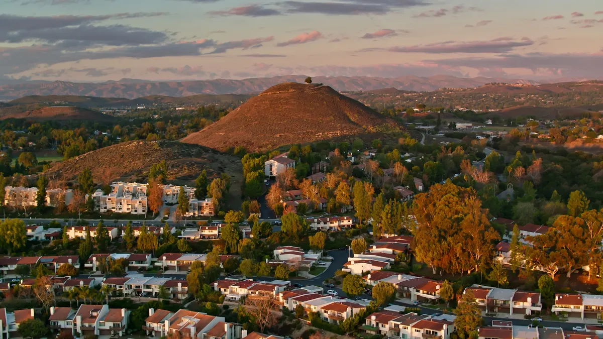 Aerial view of a hill in Thousand Oaks, California at sunset. There is a single tree a the top. Several apartment buildings are in the foreground, along with trees.