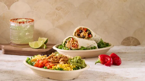 A molded fiber bowl containing salad. sits on a counter next to a molded fiber container holding a burrito.