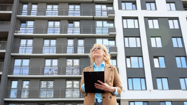 Woman making notes on clipboard with apartment building in the background.