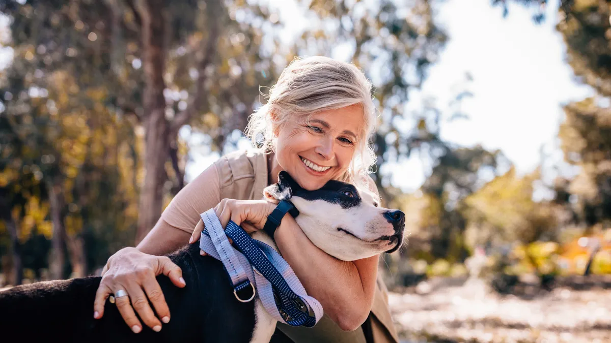 Happy woman enjoying walk in nature and embracing pet dog in forest park