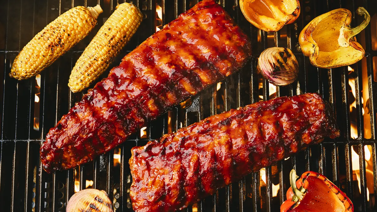 A pair of glazed pork ribs sit on a blazing charcoal grill.
