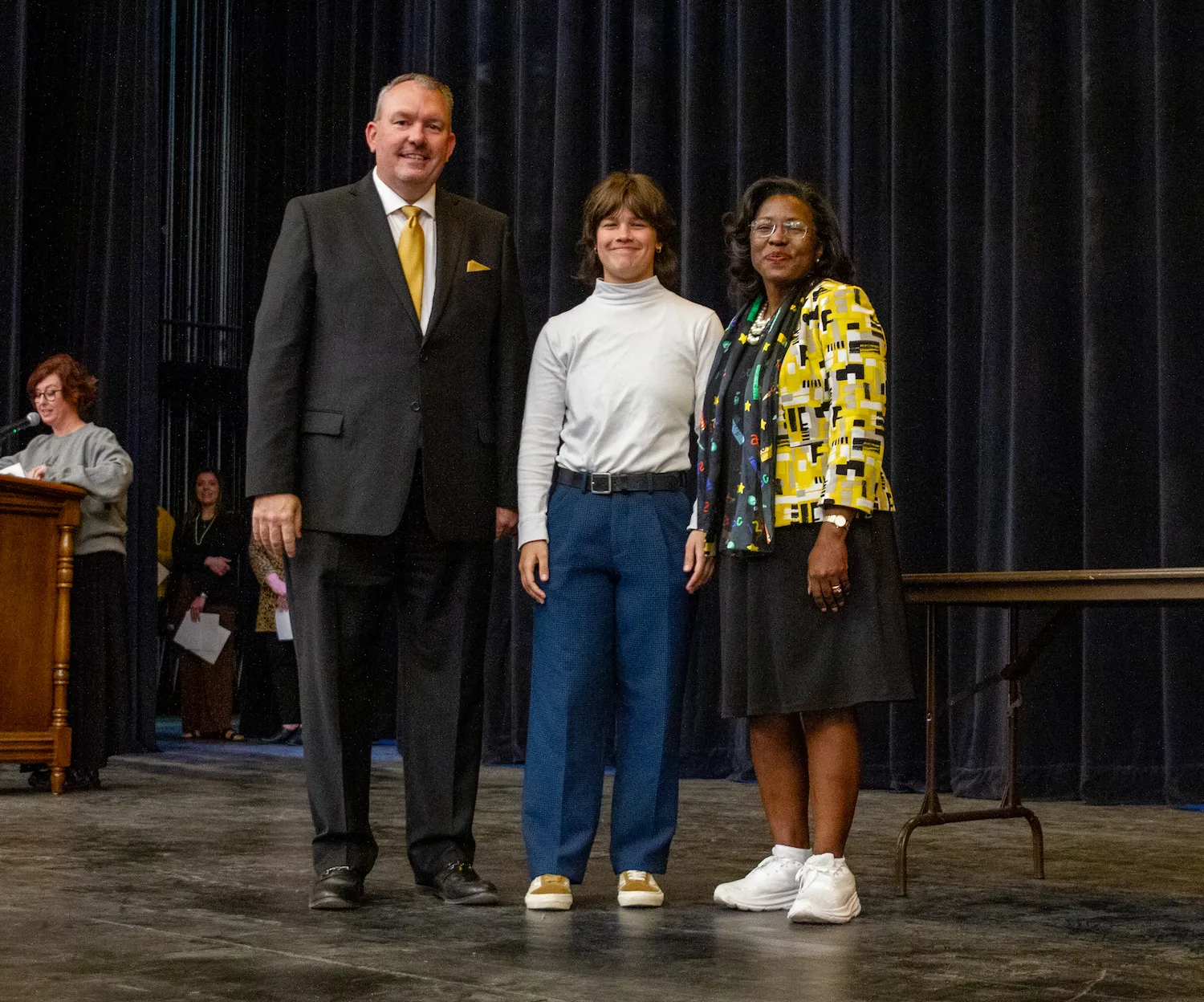 Topeka Lead High School Principal Dustin Dick and Superintendent Tiffany Anderson stand on either side of a high school senior at an event.