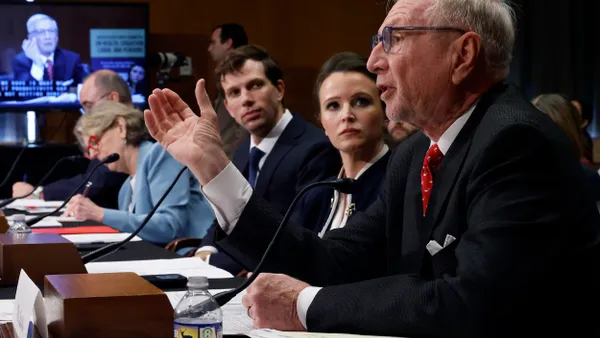 A man on the right wearing glasses testifies before Congress while a row of people to his left watch.