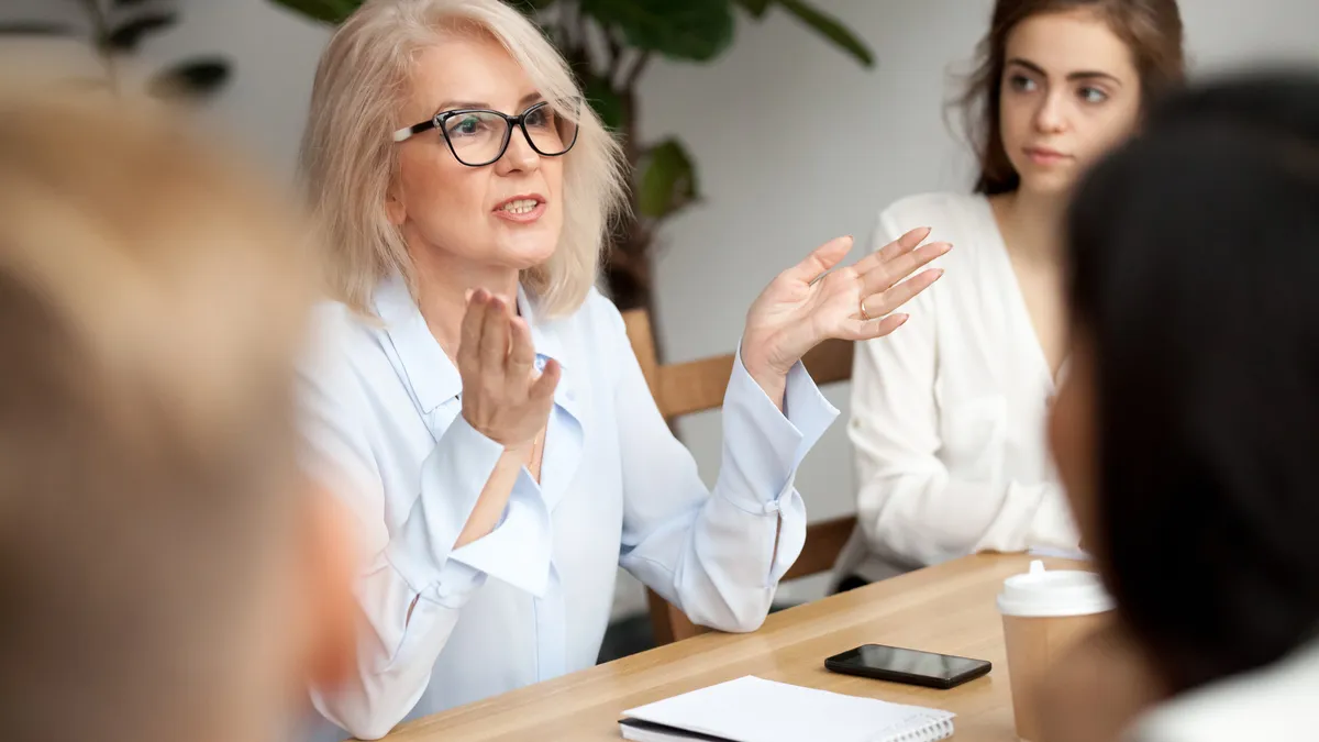 A businesswoman, teacher or mentor coach in glasses speaks to young people in a meeting or training seminar.