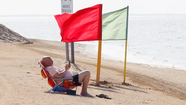 An individual sits on the beach, looking at a mobile phone.