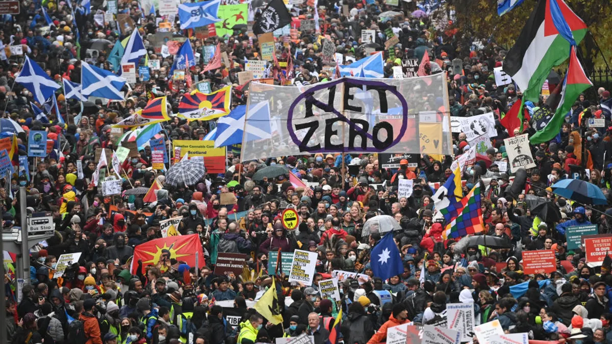 A group of people holding various flags including one that reads "Net Zero"