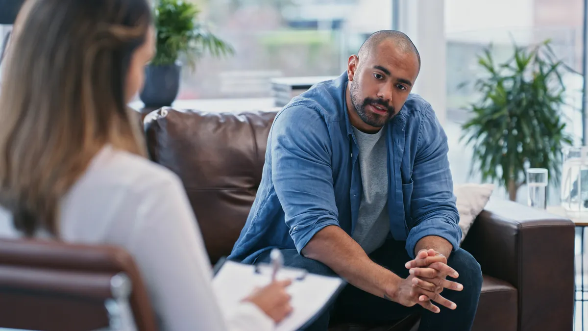 A man sits on a couch in a counseling session with a female therapist.