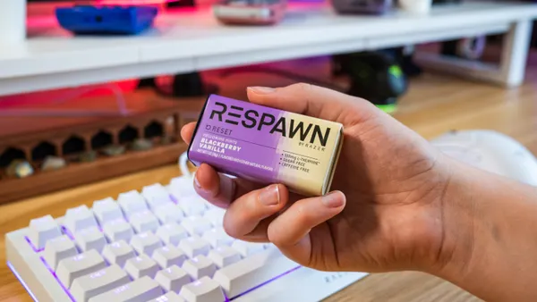 A hand holds a pack of Respawn mints in a purple and white gradient package Infront of a white gaming keyboard.